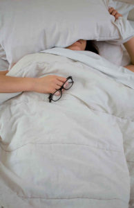 woman laying in bed, pillow over head with glasses in hand
